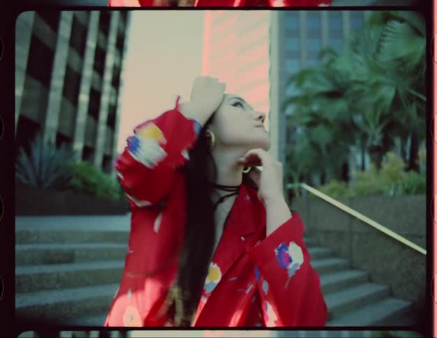 A woman gazes into the camera while dancing in front of a large building in a metropolis during the day