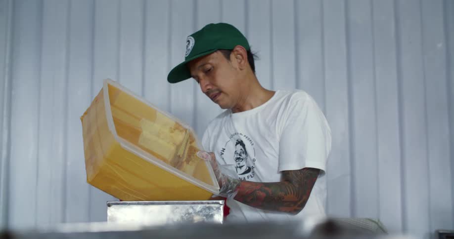 Worker pouring the contents of a yellow plastic container on a tray by hand
