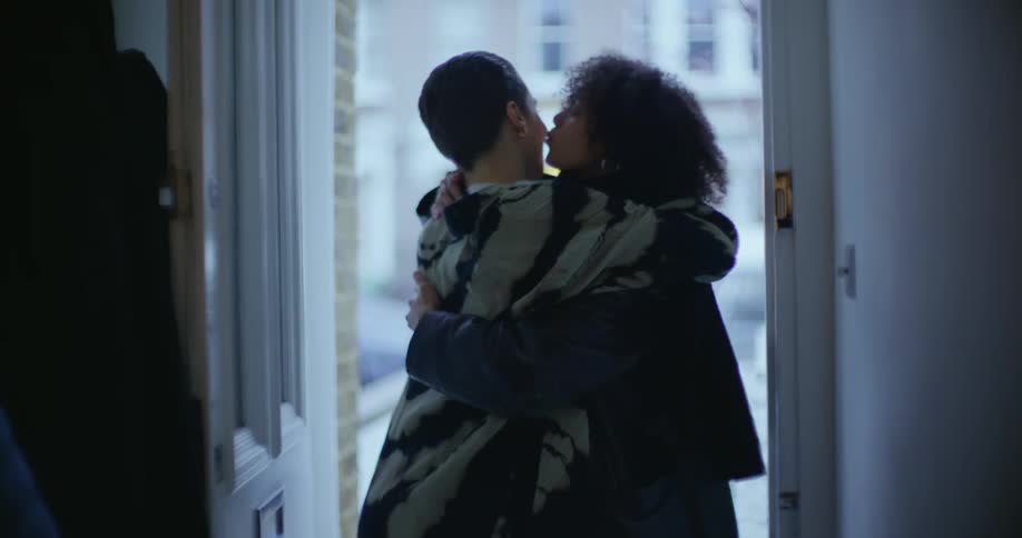 A woman opens the front  door to a good friend and they hug