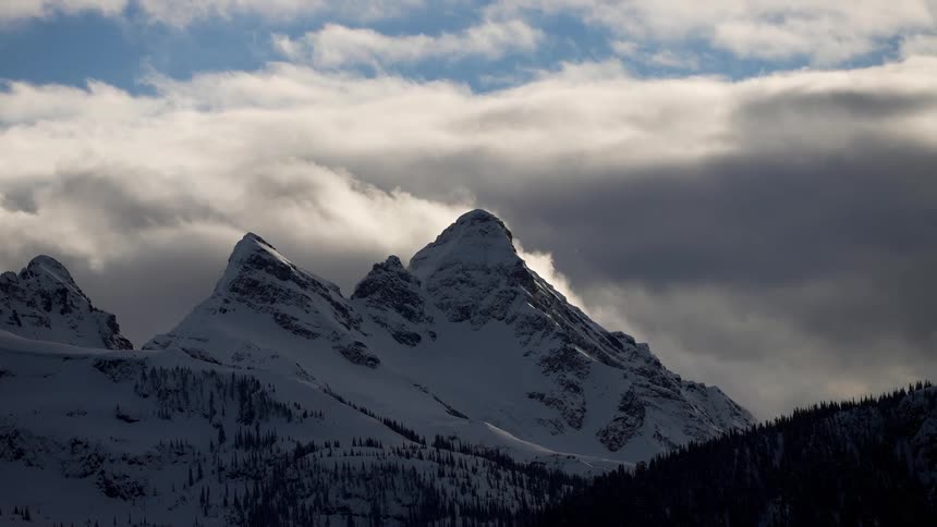 Dense clouds move past a snow capped mountain range