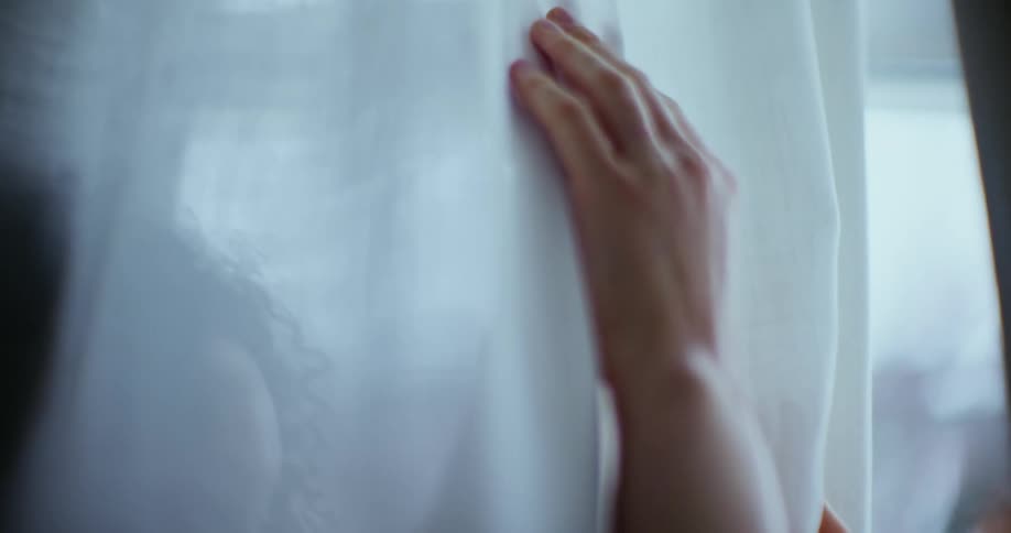 Two female hands touch through a sheer curtain