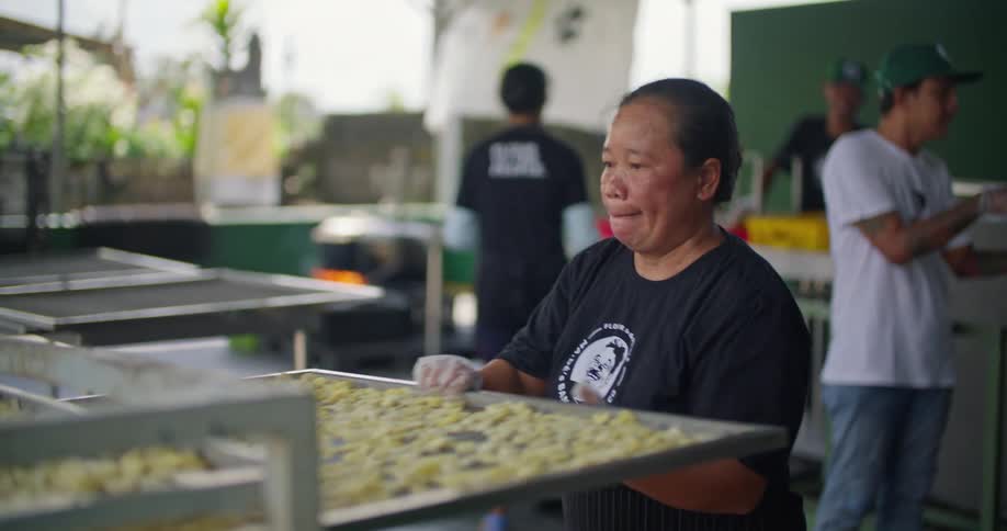 A woman places a tray of food in a rack while other workers move behind her