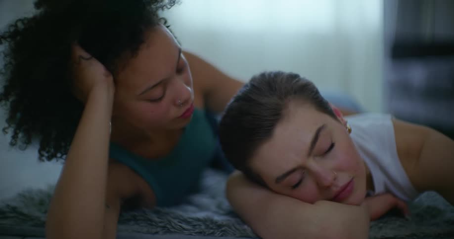 A woman caresses her girlfriends shoulder while she sleeps