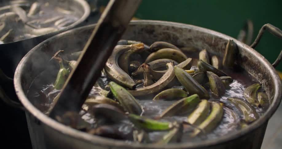 Large pots of bananas are cooking and stirred with a stick