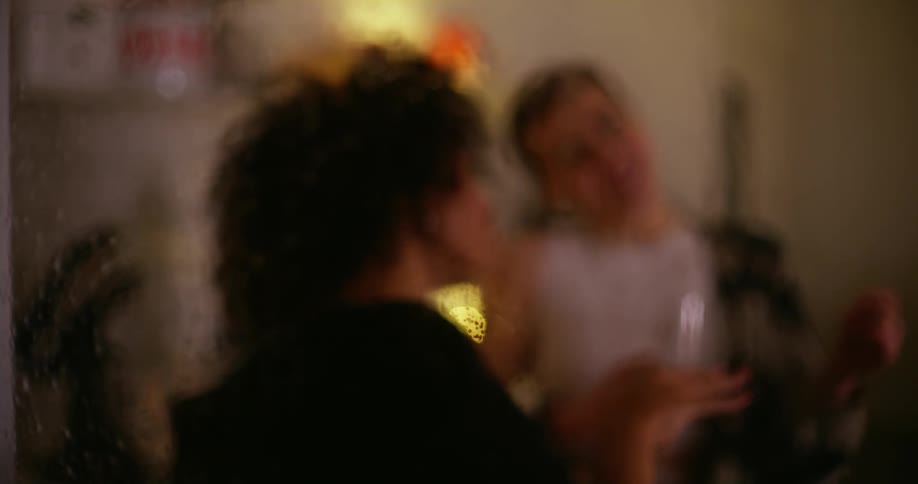 Two women dancing in a room, seen through a rain speckled window