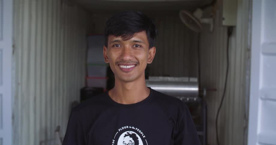 A young indian teenager is smiling and inside of his room
