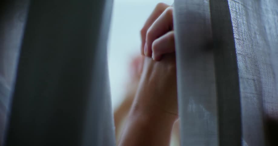 Hands clasped together behind a sheer curtain
