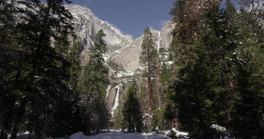 Trees standing in front of mountains that are somewhat snow-covered