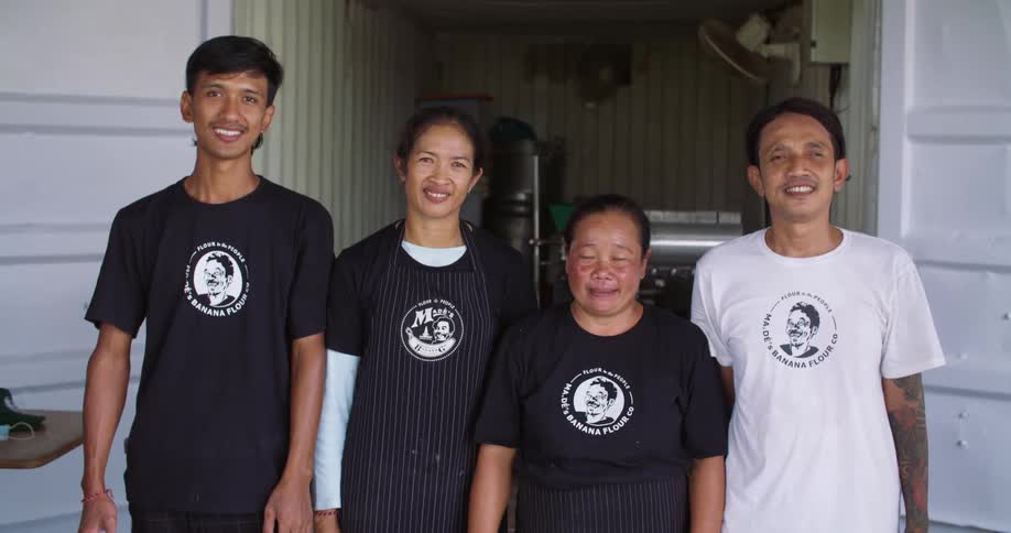 Four people smile while posing in matching shirts in front of a storage room