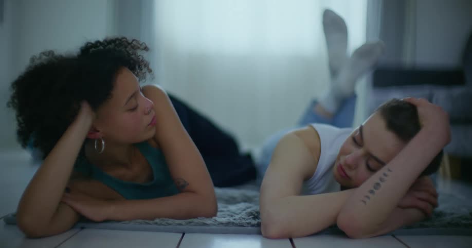 Two women lying side by side on the floor gazing at each other