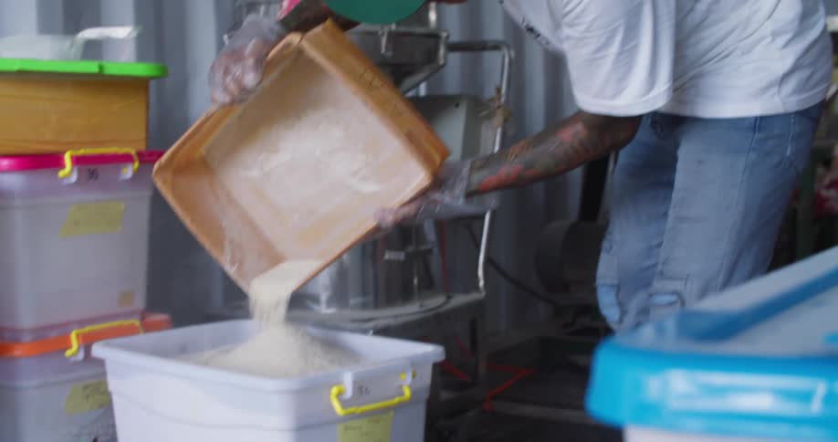 Worker fills a plastic container with flour inside a warehouse