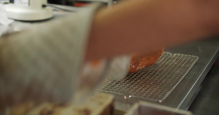 A baker takes fresh loaves of bread out of the molds and places them on a rack