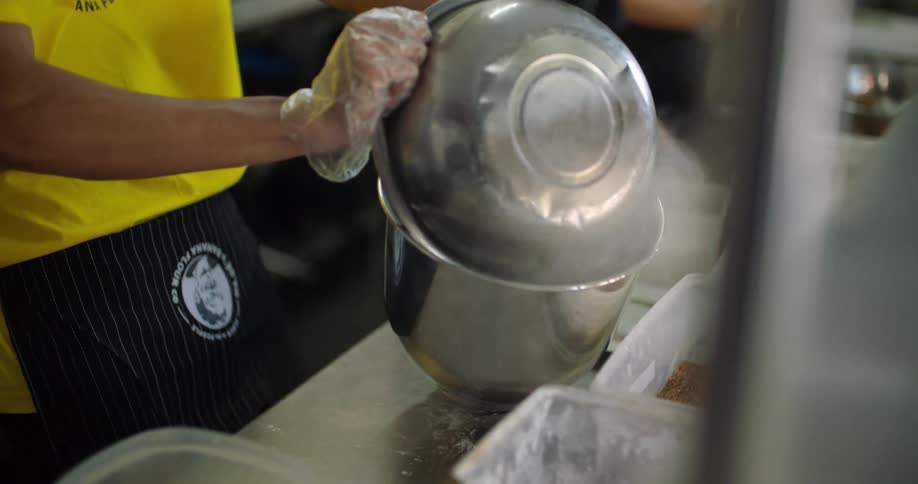 A restaurant cook transfers flour into a larger mixing bowl