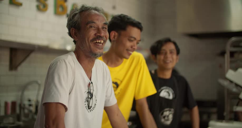 A man and two teenage boys are standing together behind a counter in a kitchen talking and laughing
