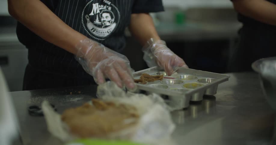 Person presses dough into cups while working in restaurant kitchen
