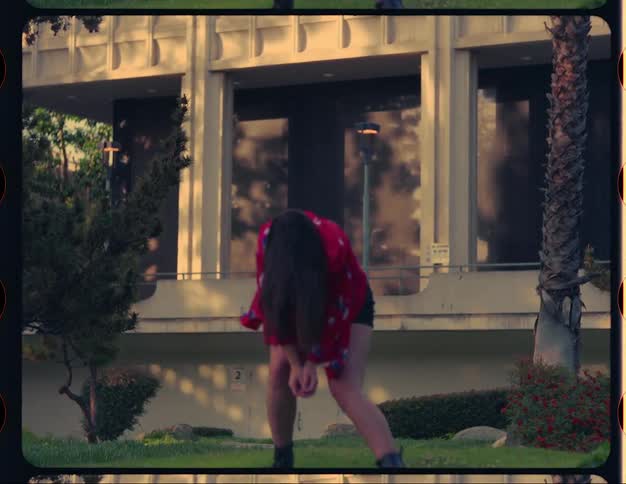 A teenage girl is standing outside of a building dancing near a tree
