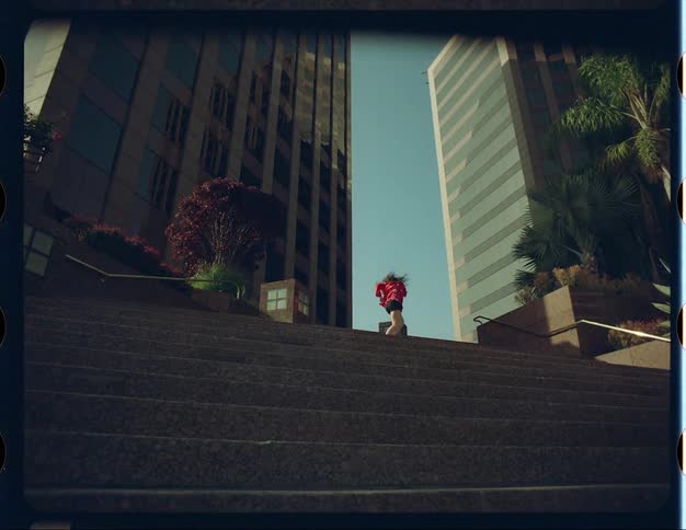 A teenage girl is dancing at the top of stairs near a downtown street and there are tall buildings behind her