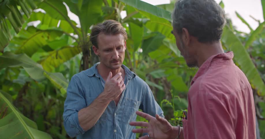 A man holding green bananas gestures as he talks discussing agriculture