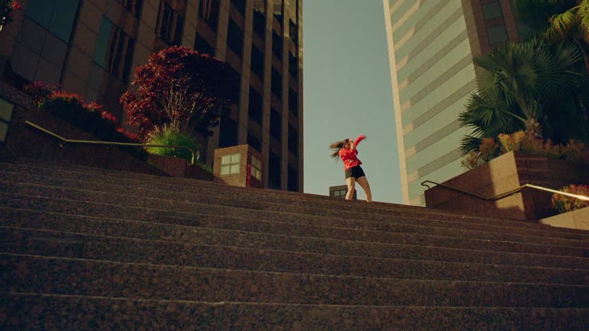 Female dancer dances at the top of the stairs that are at the base of a skyscraper