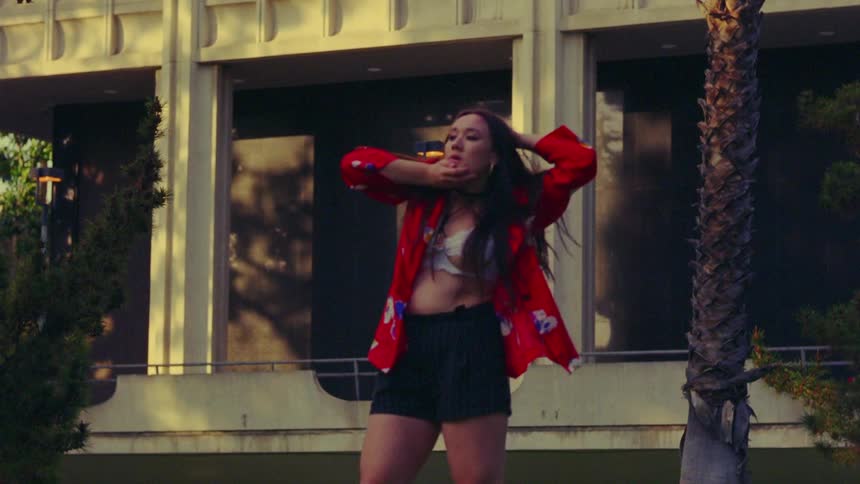 Young woman wearing a colorful jacket dancing outdoors in front of a building