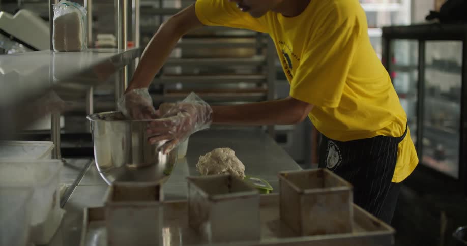 A man is scooping dough out of a bowl in a restaurant kitchen