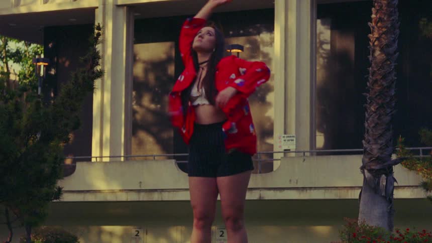 A woman standing outside reaching her arm above her head in a dance pose