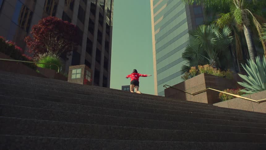 A woman dances at the top of plaza steps with office buildings behind her