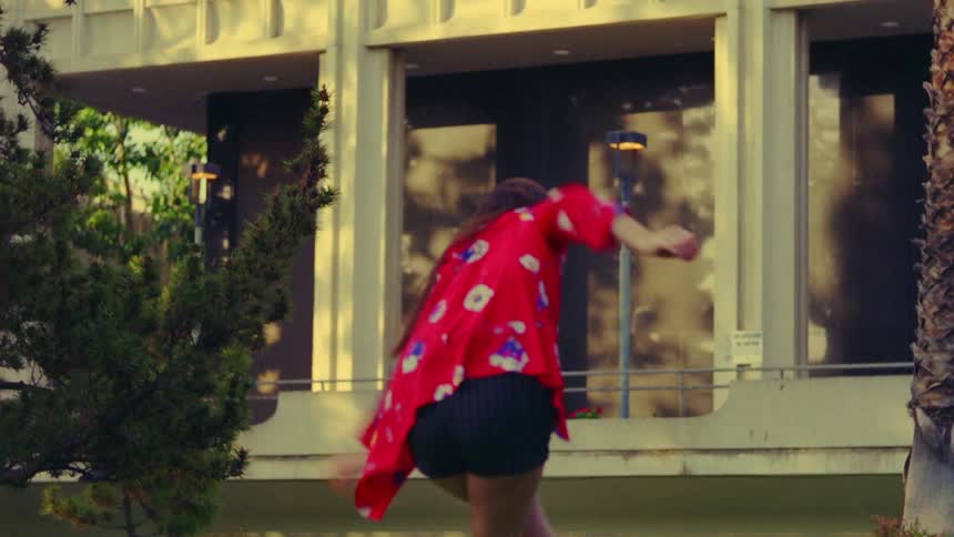 A woman is outside next to a building dancing