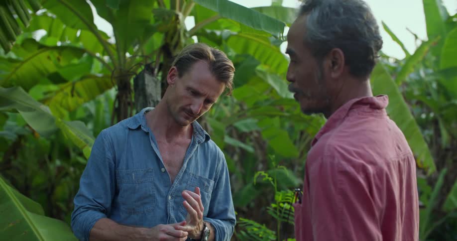 Two men talk by the banana plants
