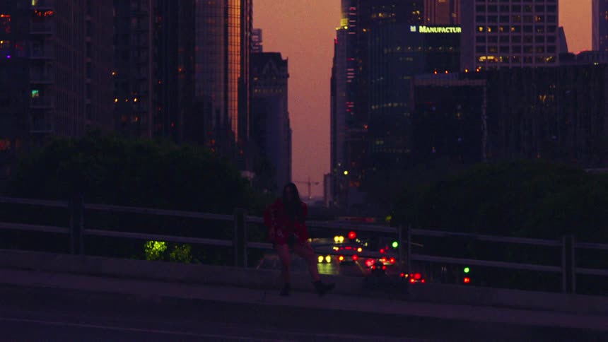 A woman is dancing on the sidewalk of a bridge in a large city