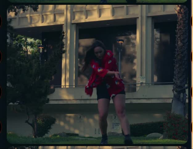 A woman dancing next to a palm tree and in front of a building