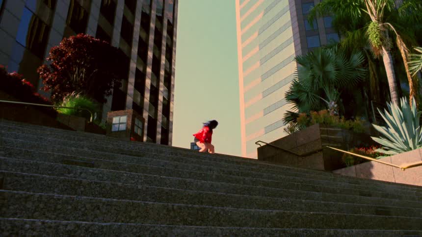 A woman dancing at the top of plaza steps in a city on a sunny day