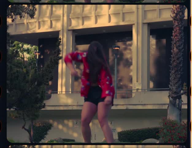 A younger white woman is dancing outside by some buildings