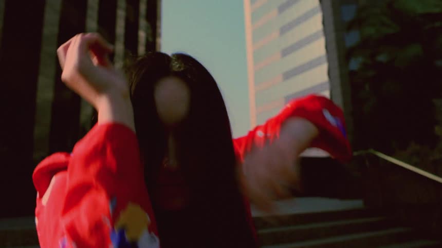 A young woman looks into the camera while dancing outdoors during the day
