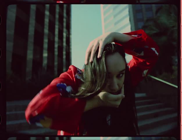 Woman moves through dance poses near steps with skyscrapers in the background