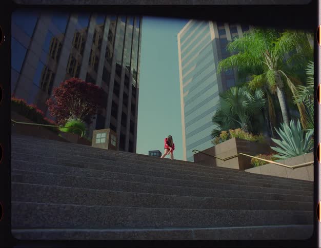A woman dances at the top of a staircase in front of large building in a metropolis during the day