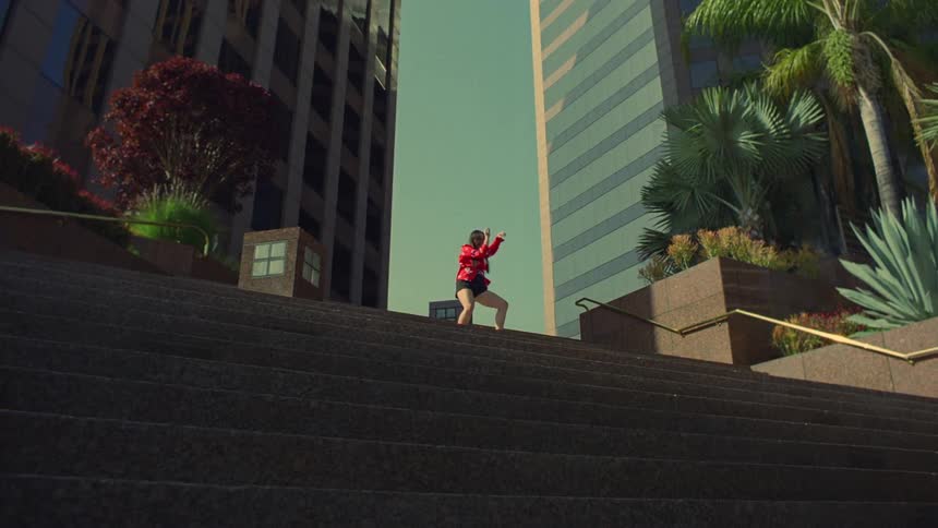 A woman is dancing at the top of stairs that lead to skyscrapers