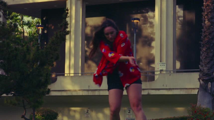 A woman dances in front of a building near a palm tree
