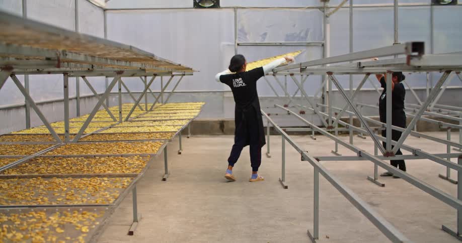 Workers place metal trails filled with plantain chips on racks fro drying inside a warehouse