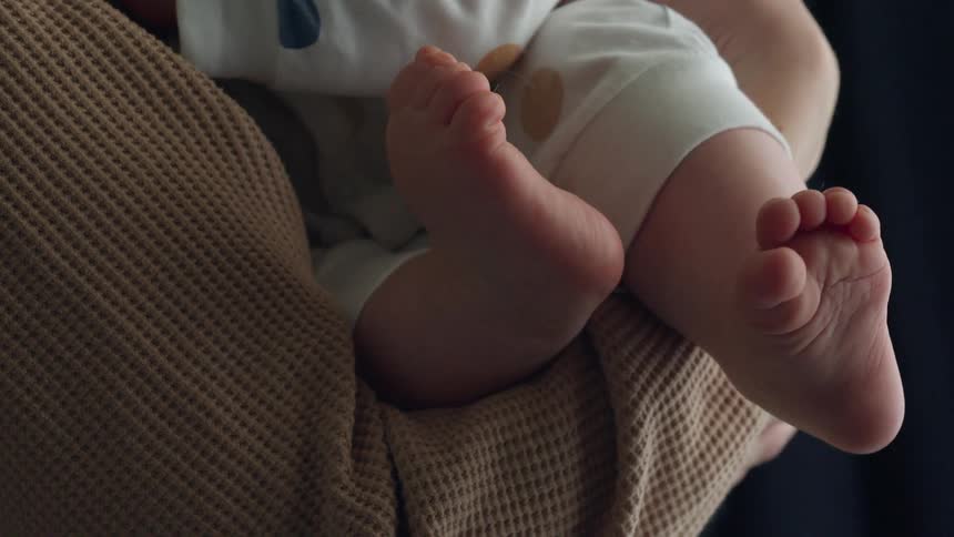 Babys chubby legs and little feet and toes move as he squirms in moms arms