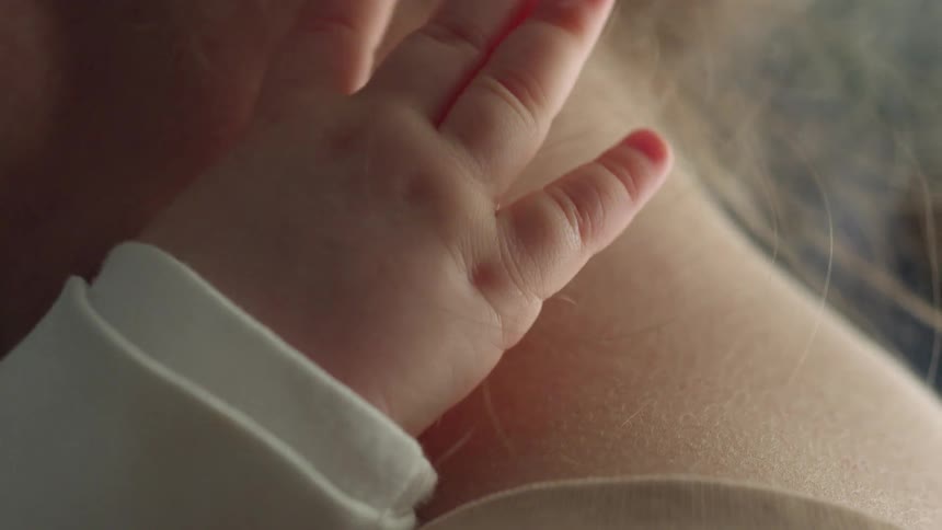 A baby touches its mothers neck while being held