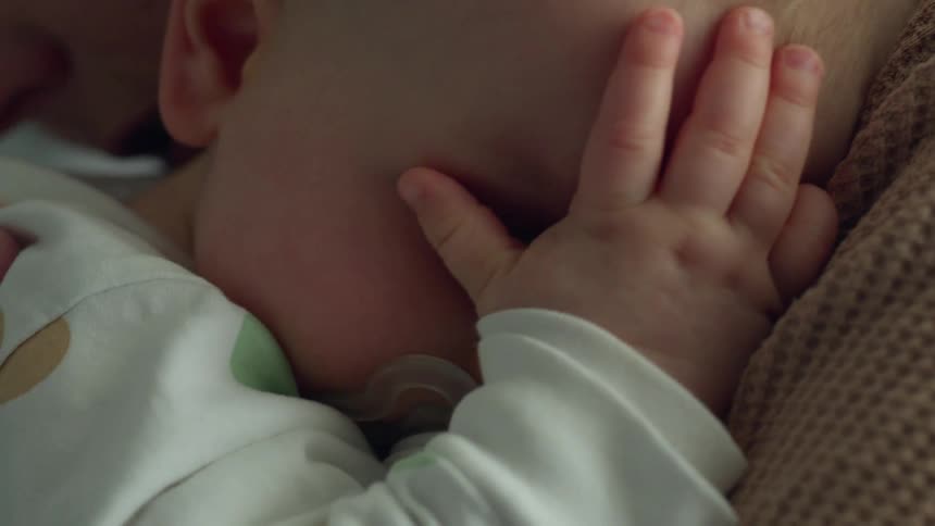 Parent holds baby sucking on a pacifier