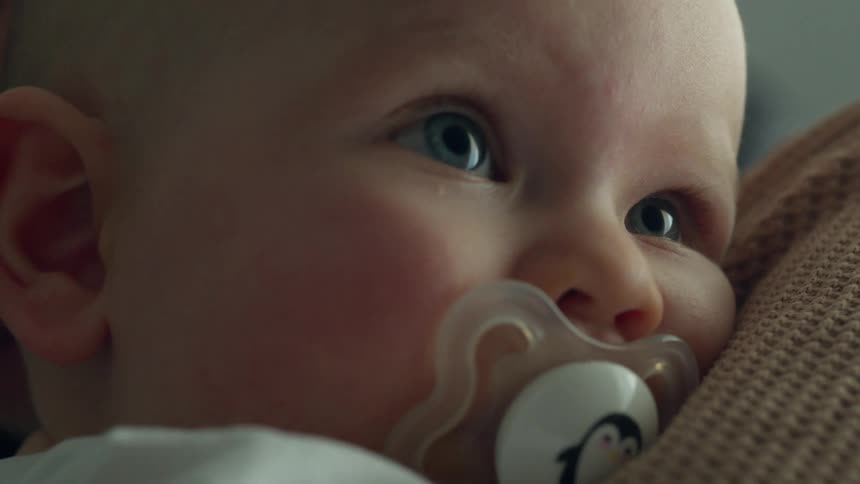 Baby looking up at mom as she rubs his back holding and cuddling him