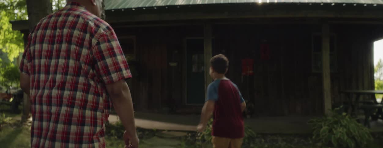 A little boy is running to the porch of a cabin and his grandfather is following him