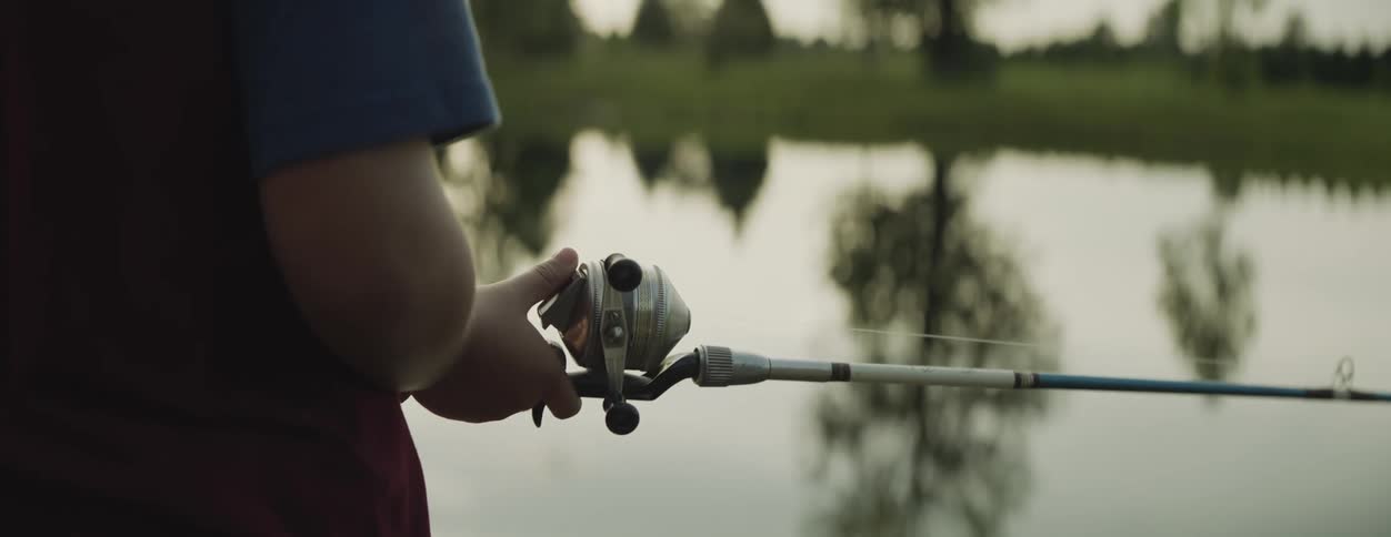 A man is holding a fishing rod and reel as he casts his line into a pond