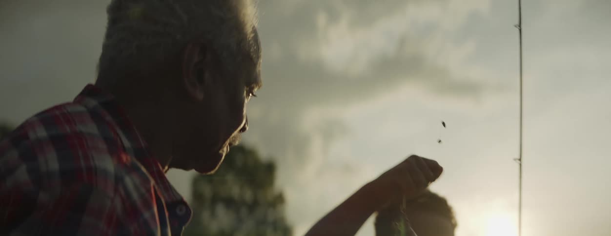 A boy is fishing with his grandfather and they are looking at the big fish on the line they just caught