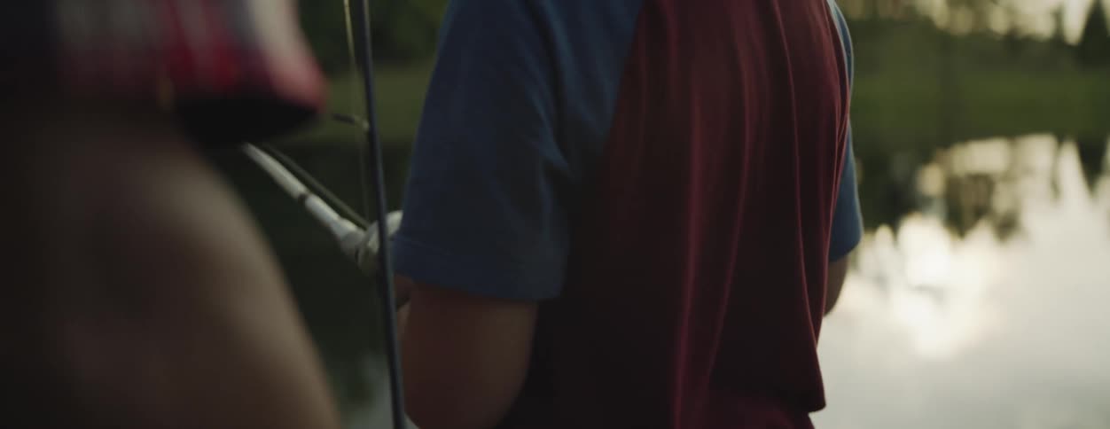 A boy reels in his line while fishing at a lake