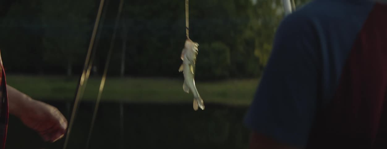 A man reaches his hand out to grasp the line and the fish his son caught at the lake