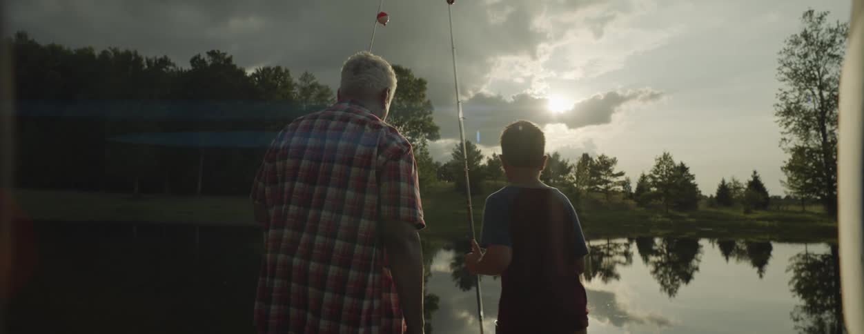 Father and son are outside holding fishing rod by a lake