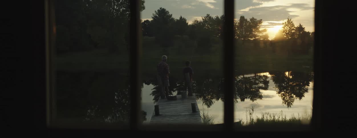 A man standing on a lake dock with his grandson fishing at dawn